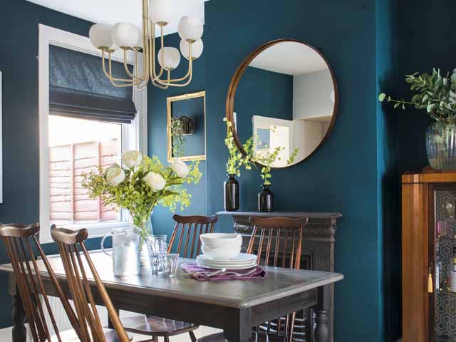 a dining room featuring a round mirror, modern and mid century furniture and teal green walls