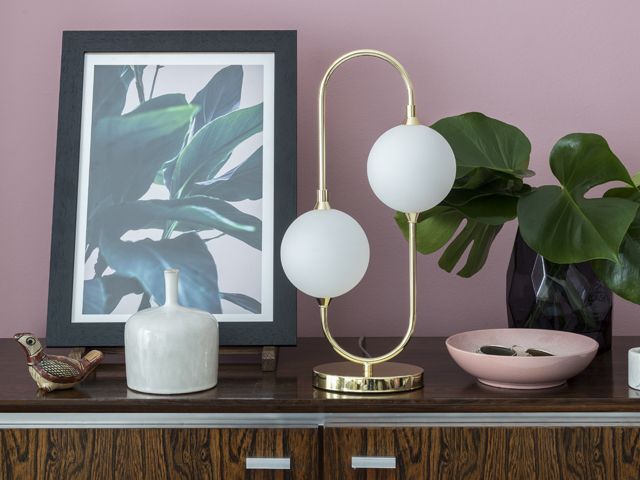 art deco style lamp on a dark wood sideboard with a plant and artwork in front of a pink walls by bhs spring summer 2018