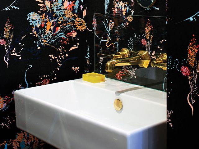 black wallpaper with jellyfish print by Pippa Jameson in a bathroom with a white sink and gold taps