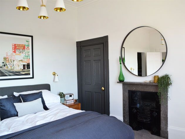 grey and white bedroom interior with large circular mirror above fireplace