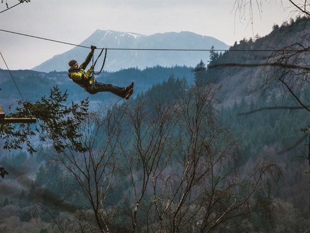 man zip lining above forest at zip world north wales