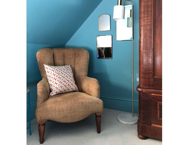 brown armchair with red and white cushion next to brass floor lamp and mirrors in teal bedroom