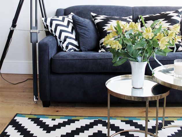 living room with velvet ink blue sofa geometric cushions and rug with yellow flowers on coffee table