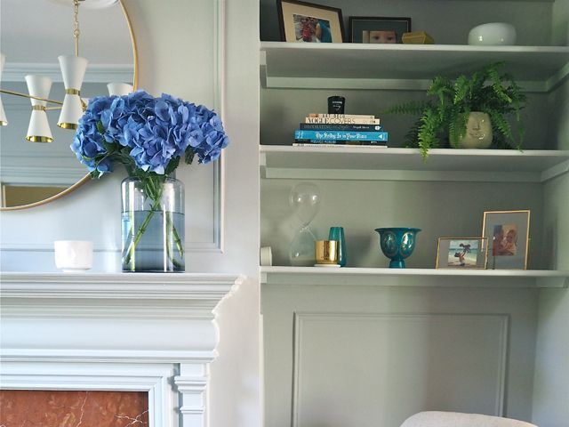 melanie lissack, interiors blogger's newly refurbished tv room with gold rim mirror, white shelving and blue hydrangea in a vase