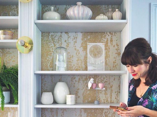 Melanie Lissack interior design blogger, in front of her revamped shelving unit with various home decor accessories