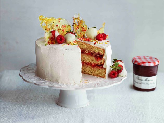 showstopper strawberry sponge cake with cream and fruit topping on white cake dish