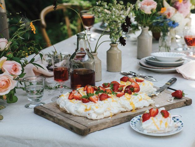strawberry lemon and elderflower pavlova on outsode dining table surrounded by roses and drinks