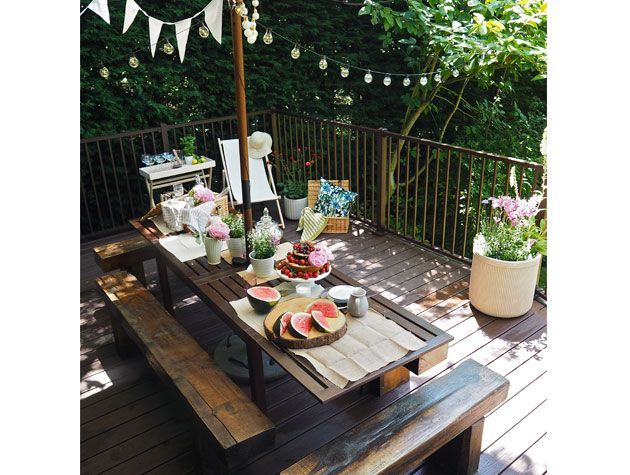 garden decking with wooden garden table decorated with flowers cake fruit and fairy lights