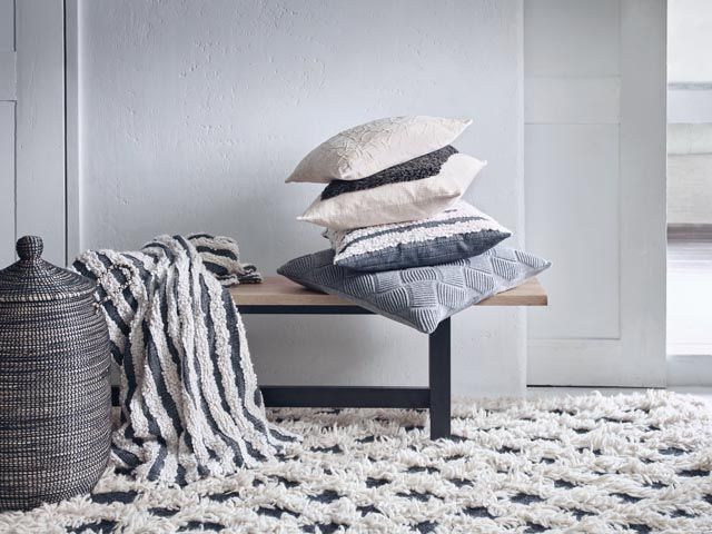 black and white textured textiles and mismatched cushions on a long bench-habitat-home-living-room-goodhomesmagazine.com