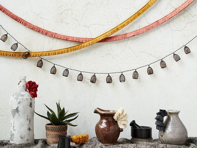 Display of jugs, plant pots and ornaments on table with fringed material from Hillarys and Abigail Ahern's curtain and Roman blinds collection-livingroom-goodhomesmagazine.com