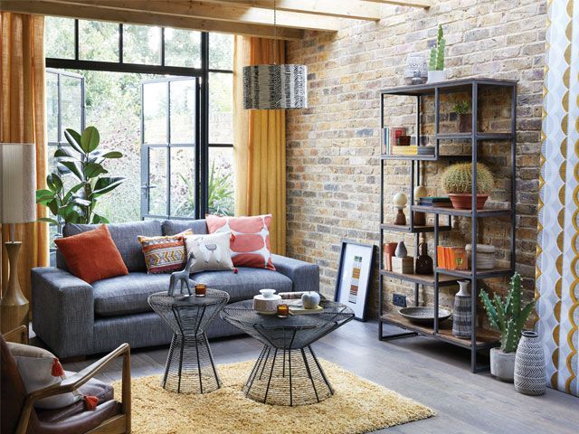 Living room with brick wall grey sofa, wicker coffee table and yellow curtains -dunelm-living-room- goodhomesmagazine.com