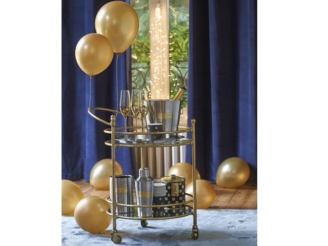 Gold bar trolley with champagne flutes, an ice bucket, gold balloons and cocktail shakers -maisons-du-monde-living-room-goodhomesmagazine.com