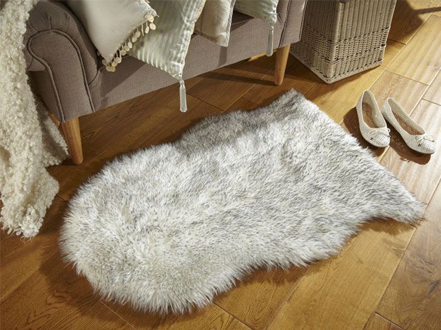 Grey sheepskin rug in a living room with a grey sofa and decorative beige pompom cushions -the-rug-seller-libing-room-goodhomesmagazine.com