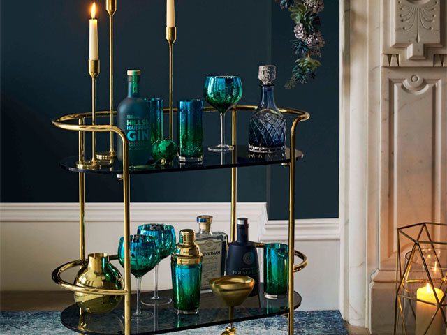 a gold trim bar cart with cocktail accessories in a teal blue living room from John Lewis AW18