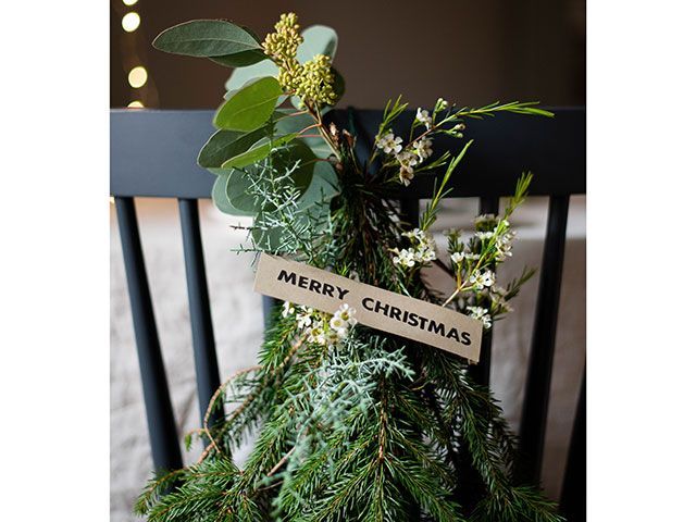 foliage and branches on a black dining chair with Merry Christmas wooden sign - christmas foliage styling ideas - living room - goodhomesmagazine.com
