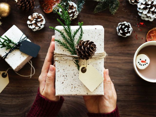 Hands holding anonymous Christmas present tied with an acorn eucalyptus -pexels-shopping-goodhomesmagazine.com