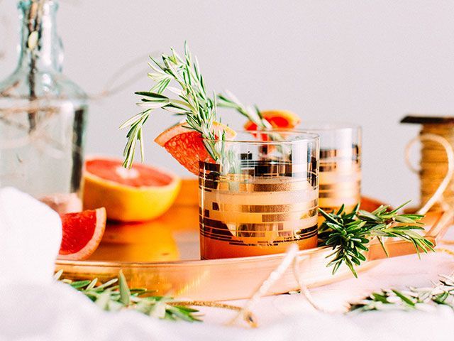 orange cocktails in gold rimmed glasses with party accessories and cocktail garnishes - how to throw a new year's eve party - goodhomesmagazine.com