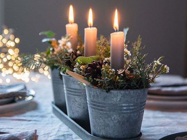 plants in three metal pots with candles on a dining table - Christmas foliage styling ideas - goodhomesmagazine.com