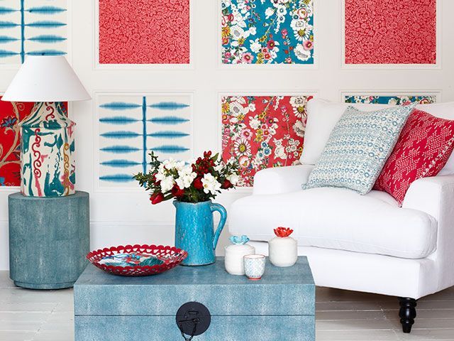 An eclectic blue and red living room with squares of wallpaper framed on the wall with wooden beading