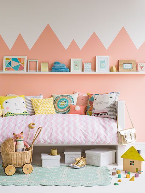 A children's pastel-themed nursery with prints on a picture rail and a geometric painted wall