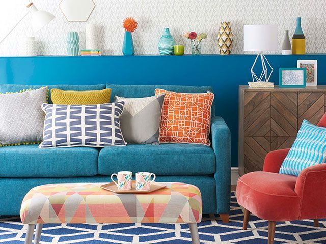 Blue sofa in a modern living room with a geometric footstool and patterned cushions plus a half wall shelf