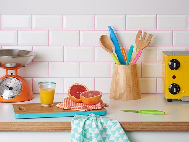 A retro kitchen with retro pastel accessories and white tiles, finished with bright pink grout