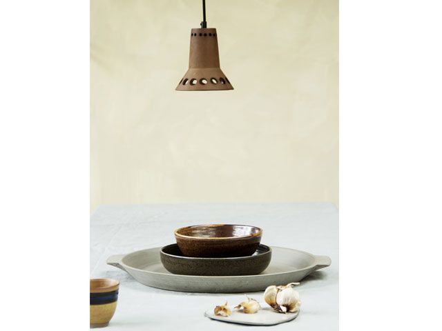 Stacked grey and brown plates on dining table with a brown ceiling lamp shade hanging above -trouva-living-room-goodhomesmagazine.com