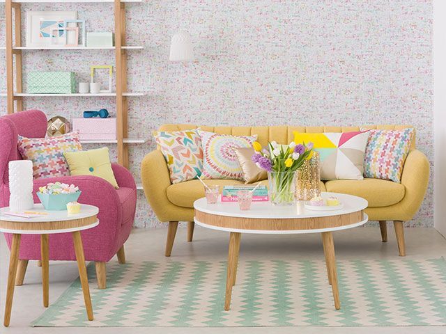 Midcentury modern living room with a yellow sofa and pink armchair, both with geometric cushions in pastel shades, surrounded by Fifties furniture in a Scandi style