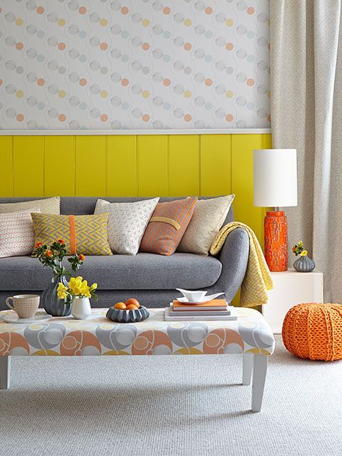 Grey sofa with a mix of coral and tangerine coloured cushions, decorated with half-walled yellow panelling and spotty wallpaper,