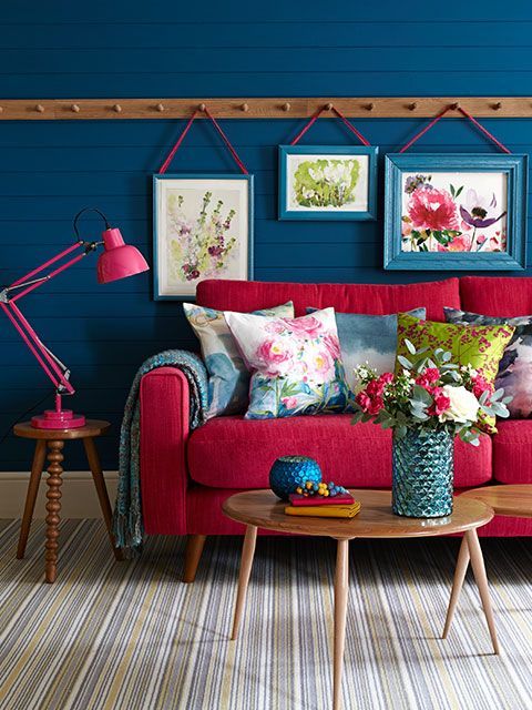 Bright, pink sofa with painterly pink and blue cushions, against a blue panelled wall with peg rail and hanging pictures