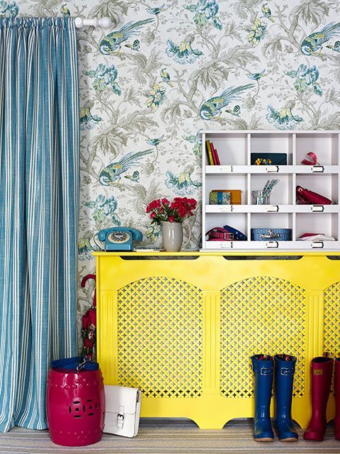 Bright yellow radiator cover in a country-style home with statement bird wallpaper and blue striped curtains