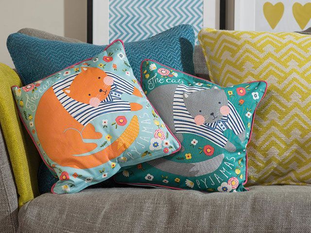 Two cat cushions in bright orange and blue on a grey sofa