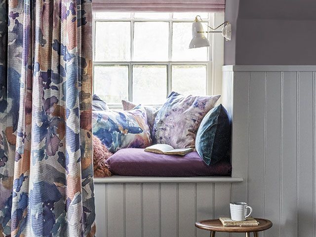 A tongue and groove window seat decked out with purple cushions in a painterly style