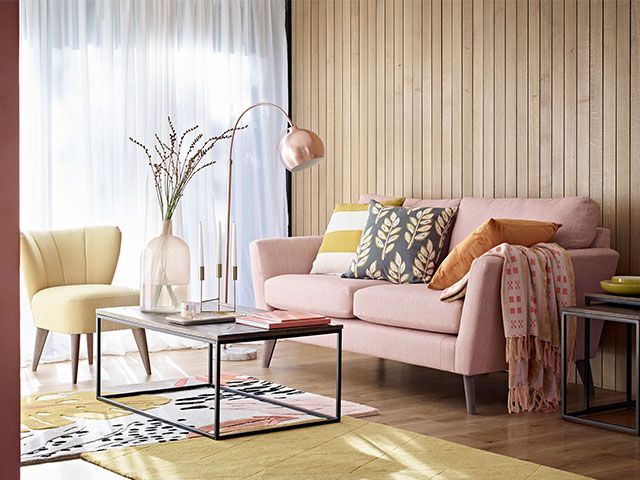 A Scandi-style living room with wooden panelling, a millenial pink sofa, a yellow rug and copper accents