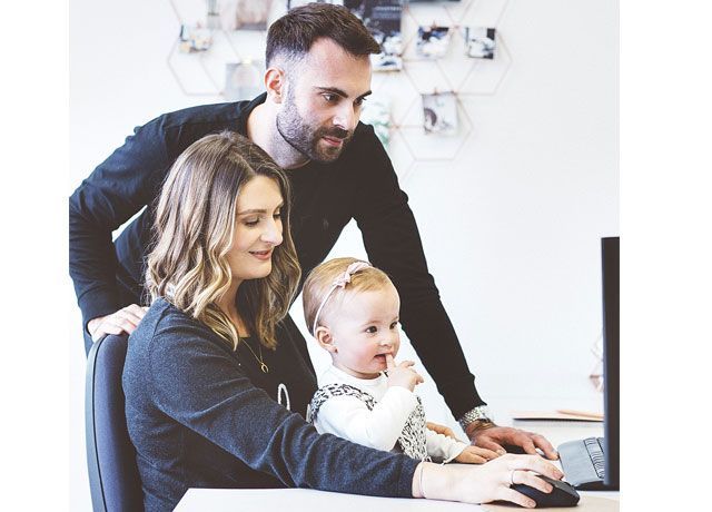 Becky Broome sat with her daughter on her lap and her husband standing next to her in from of a computer -notonthehighstreet-living-room-goodhomesmagazine.com