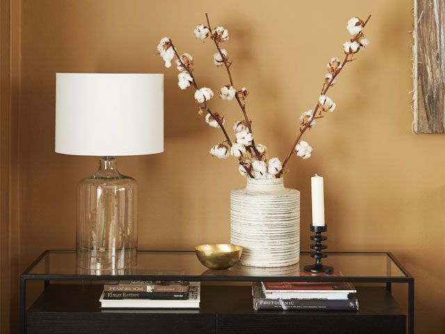 Mantelpiece with glass lamp and faux flowers in a Dulux Spiced Honey living room - living room - goodhomesmagazine.com