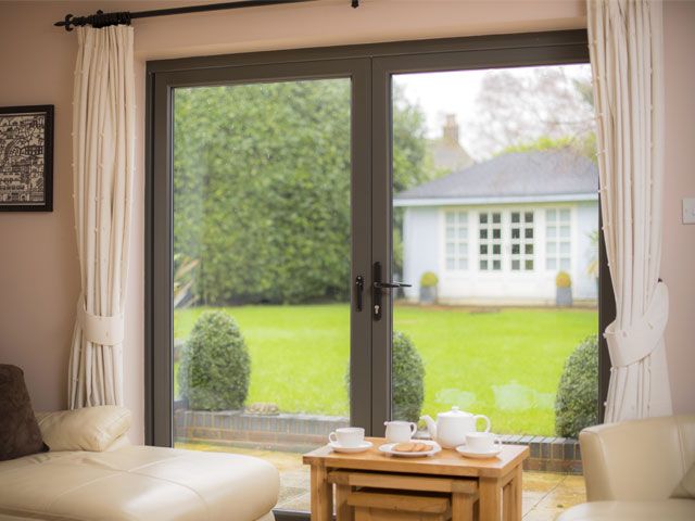 A pink painted living room with french doors with a grey door frame that look out on to a garden -origin-living-room-goodhomesmagazine.com