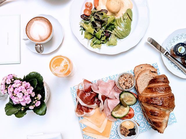breakfast consisting of avocado toast, croissant, meats, cheese and coffee on a table with a white tablecloth