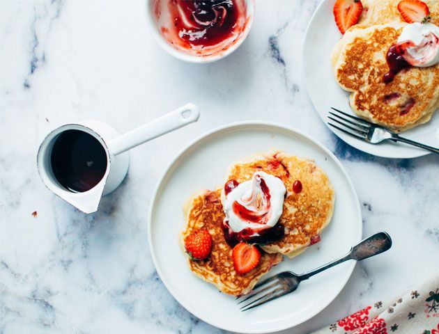 Pancakes topped with strawberries, cream and strawberry jam served on a white plate and place on a marble dining table -unsplash-living-room-goodhomesmagazine.com