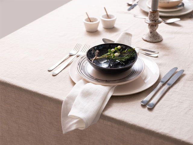 Picture of a dining table dressed with a white table cloth, stacked white plates and a blue bowl -trouva-living-room-goodhomesmagazine.com