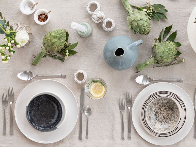 A table setting with scattered green foliage, white plates, blue bowls -trouva-living-room-goodhomesmagazine.com