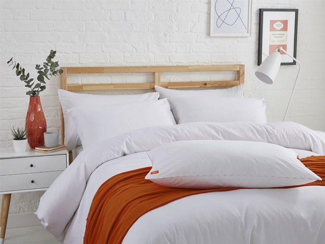Picture of a white brick bedroom with a Nanu bed with white bedding and an orange throw -nanu-bedroom-goodhomesmagazine.com