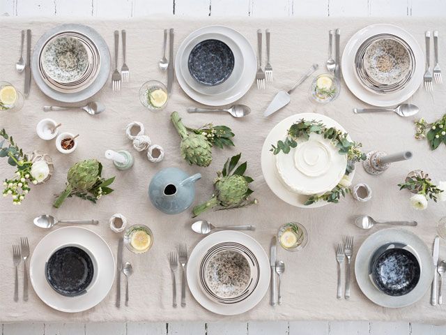 A white wooden dining table dressed with a white table cloth, green foliage and blue bowls -trouva-living-room-goodhomesmagazine.com