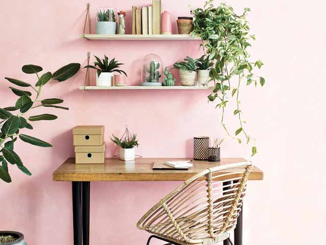 Stylish workspace home office with pastel pink wall, rustic shelves and desk, rattan desk chair and plants - goodhomesmagazine.com