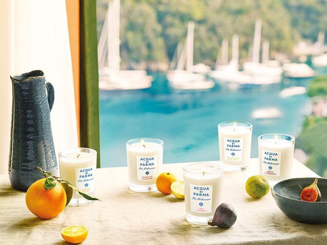 NEW Acqua di Parma Home candle collection positioned in front of a window looking out on to an Italian seaside scene