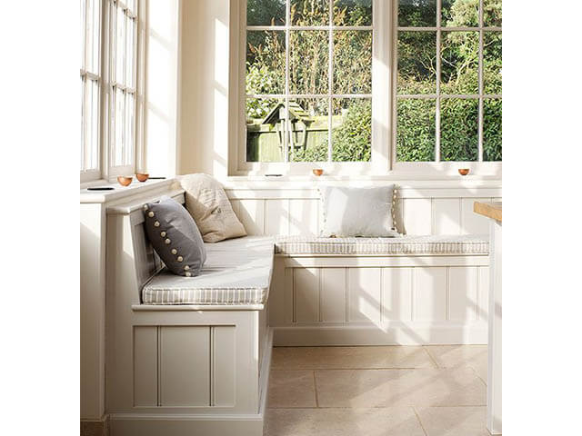 airy white orangery with window seats and large windows overlooking mature garden