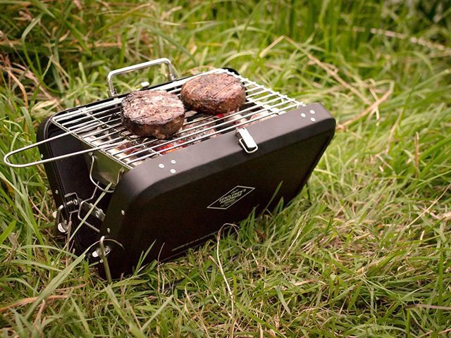Portable barbecue cooking burgers in a field of grass