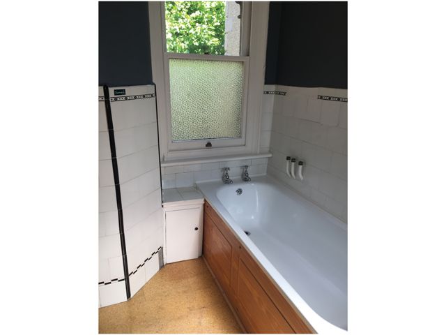 old bathroom in a terrace house with white tiles and wood panelling on bath