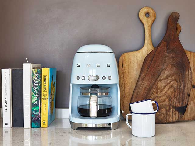 Blue Smeg coffee machines on shelf with wooden boards, mugs and cookbooks
