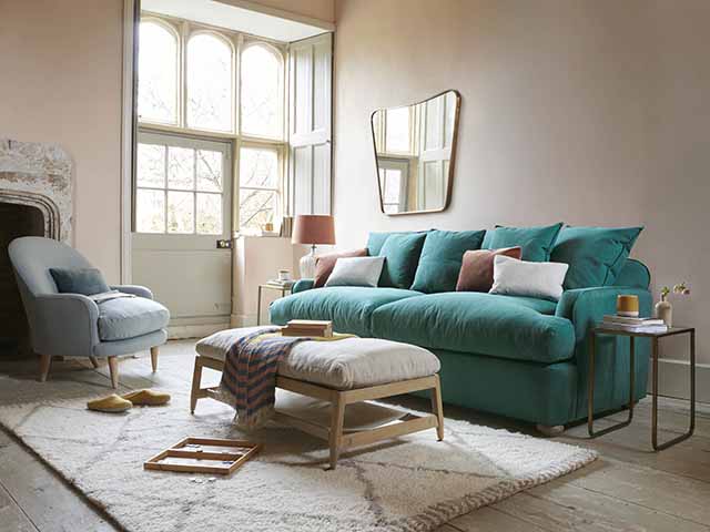 Teal sofa bed with scattered cushions and gootstool with fluffy cream rug, goodhomesmagazine.com